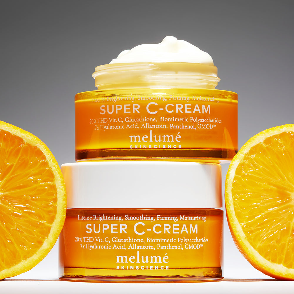 image mood of two Melume Skinscience's super c-cream stacked on top. The top super c-cream is opened showing the texture. Next to both super c-cream are oranges.